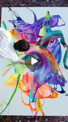 a man is painting on a large canvas with colorful paint splattered all over it