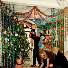 a group of people decorating a christmas tree in a living room with green garlands