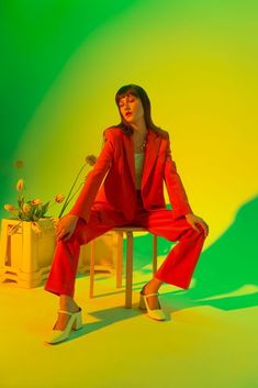 a woman sitting on top of a wooden chair next to a flower pot in front of a green and yellow background