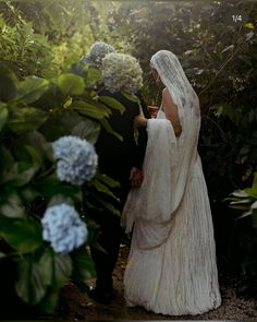 a bride and groom standing in the middle of some bushes with blue hydrangeas