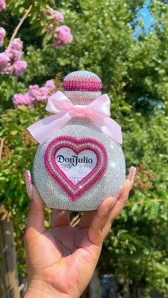 a person holding up a small bottle with a heart on it's top and a pink bow around the neck