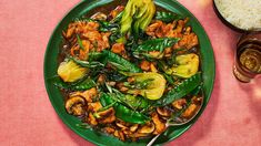 a green plate filled with meat and vegetables next to rice on a pink tablecloth