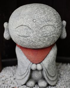 a small gray statue with eyes closed sitting in gravel