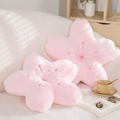 two pink pillows sitting on top of a white couch next to a cup and saucer