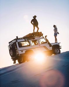 two people standing on top of a jeep in the desert