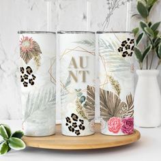 three white tumbles with floral designs on them sitting on a wooden tray next to a vase