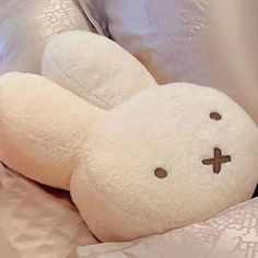 a white teddy bear with a cross on it's face laying in a bed