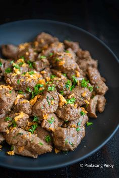 a black plate topped with meat covered in gravy and garnished with parsley