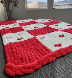 a red and white crocheted blanket on top of a bed next to a window