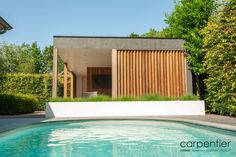 an outdoor swimming pool surrounded by greenery and wooden slatted doors on the side of a house