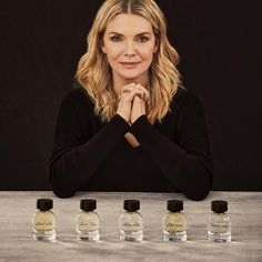 a woman is sitting at a table with five small bottles in front of her, and she's looking into the camera