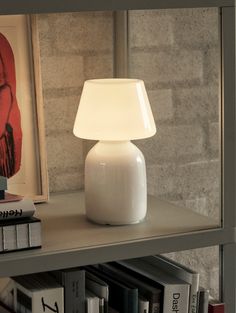 a white lamp sitting on top of a book shelf next to a bookshelf