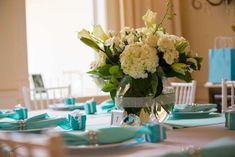 a table set with blue and white place settings, napkins and flowers in a vase