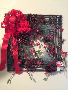 a christmas wreath with pine cones and red ribbon hanging on the wall next to a candle