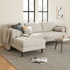 a living room with a sectional couch, coffee table and books on the floor in front of large windows