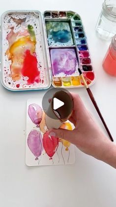 someone is painting with watercolors on paper and holding a paintbrush in their hand