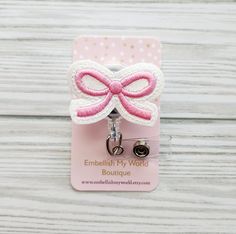 a pink and white bow clip with a name tag attached to it on a wooden background