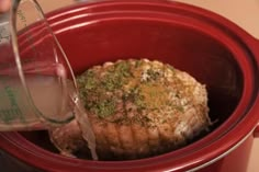 a person pouring water into a red pot filled with cooked meat and vegetables in it