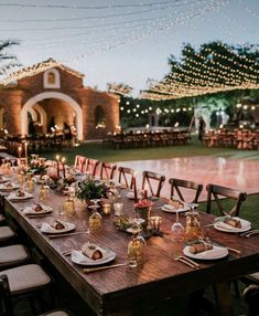 a long wooden table with plates and candles on it in front of an outdoor venue