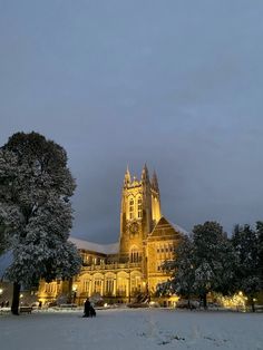 a large building that is lit up in the night with snow on the ground and trees around it