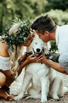 a man and woman kissing their dog with greenery on his head as he kisses the dog's face