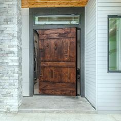 a wooden door is open in front of a white house with brick pillars and windows