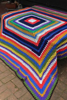 a multicolored crocheted blanket sitting on top of a brick floor next to a table