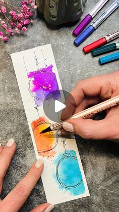 someone is drawing with colored pencils and watercolors on paper next to some flowers