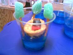 a dessert in a plastic cup on a blue table with other plates and cups behind it