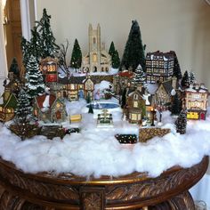 a christmas village is shown on top of a table covered in snow and fake trees