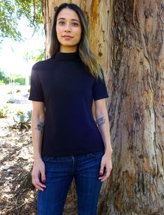 a woman standing next to a tree in front of a large, old tree with tattoos on her arms