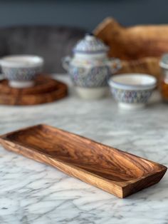 a wooden tray sitting on top of a marble counter next to cups and saucers