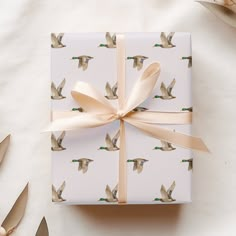 a gift wrapped in white paper with birds on it and ribbon tied around the box