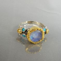 "Gold and Silver Engagement Ring, Moonstone Ring, Venus Ring, Statement Ring, Moonstone Jewelry, Antique Style Ring, Engagement Ring This unique engagement ring design, features sterling silver band and a setting of natural turquoise gems on both sides. At the center, you will find a genuine rainbow moonstone in 22K solid gold bezel. The solid gold is also hammered around the moonstone gemstone and makes this ring a true and delightful organic piece. This ring can be worn as an engagement ring o Gold And Silver Engagement Ring, Venus Ring, Engagement Ring Moonstone, Antique Style Rings, Xmas 2024, Ring Moonstone, Silver Engagement Ring, Vintage Style Rings, Jewelry Antique