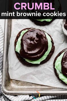 four chocolate cookies with green frosting on a baking sheet next to an empty cupcake tin