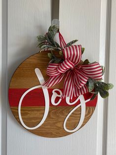 a wooden sign with the word joy hanging on it's front door, decorated with red and white striped ribbon