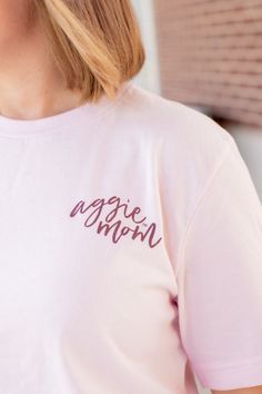 Show your Aggie pride with this stylish Texas A&M Pink Cursive Aggie Mom T-Shirt! It features a light pink shirt with "Aggie Mom" printed in maroon cursive on the left side of the chest. The back has "Aggie Mom" in darker pink with "Texas A&M University College Station" circling it - perfect for any proud Aggie Mom! - Brand: Bella+Canvas - 100% Cotton - Machine Wash Warm/Tumble Dry Low Aggie Pride, Light Pink Shirt, Texas A M University, College Shirts, Soft Pink Color, College Station, University College, Texas A&m, Colleges And Universities