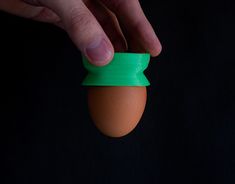 an egg being held by a hand with a green band around it's head