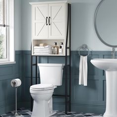 a white toilet sitting next to a sink in a bathroom under a mirror and towel rack