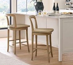 two wooden chairs sitting in front of a kitchen island with wine bottles on top of it