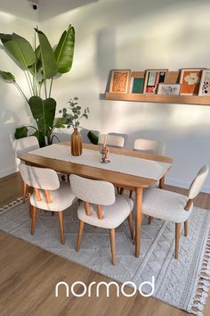 a dining room table with white chairs and a potted plant on the wall above it