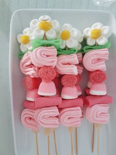 some pink and green cake pops on a white plate with flowers in the middle one is made out of marshmallows