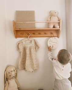 a small child reaching up to the wall with a teddy bear and other items on it