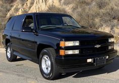 a black chevrolet suburban parked on the side of the road in front of a mountain