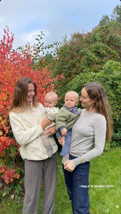 two women and a baby standing in front of some bushes