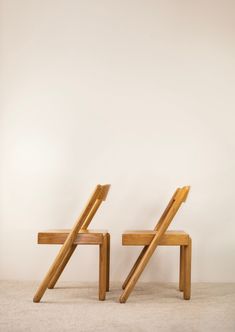 two wooden chairs sitting next to each other on top of a carpeted floor in front of a white wall