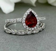 a close up of a ring with a red tear shaped stone on it and white flowers in the background