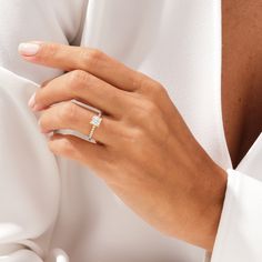 a woman's hand with a diamond ring on her left hand, wearing a white shirt