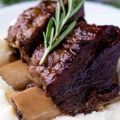 a plate with mashed potatoes and meat on it, garnished with rosemary