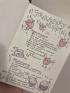 a hand holding a notebook with writing on it and strawberries in muffins